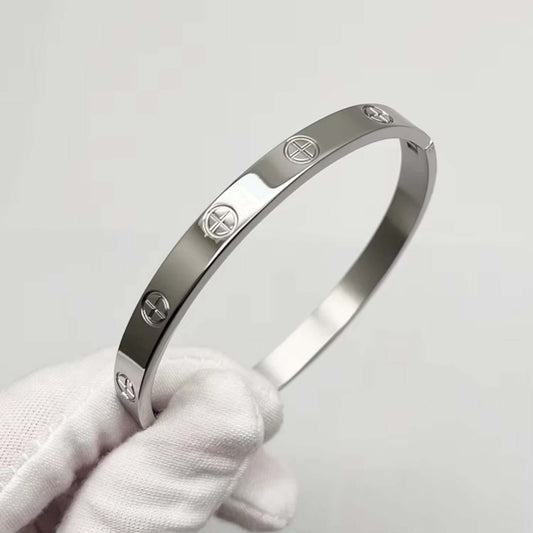 Silver bracelet with engraved logos held by a gloved hand against a light gray background